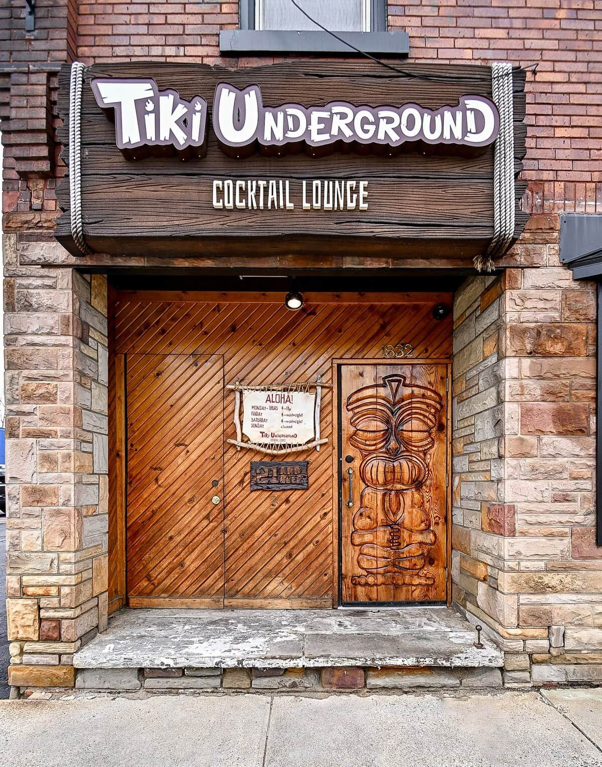 A wooden door with a sign above it that reads 'Tiki Underground Cocktail Lounge.'