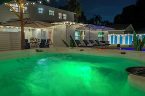 A swimming pool area with lounge chairs and umbrellas, surrounded by a house with string lights. - The Privateer, Cold Plunge, Hot Tub, Sauna + Games (Tampa)