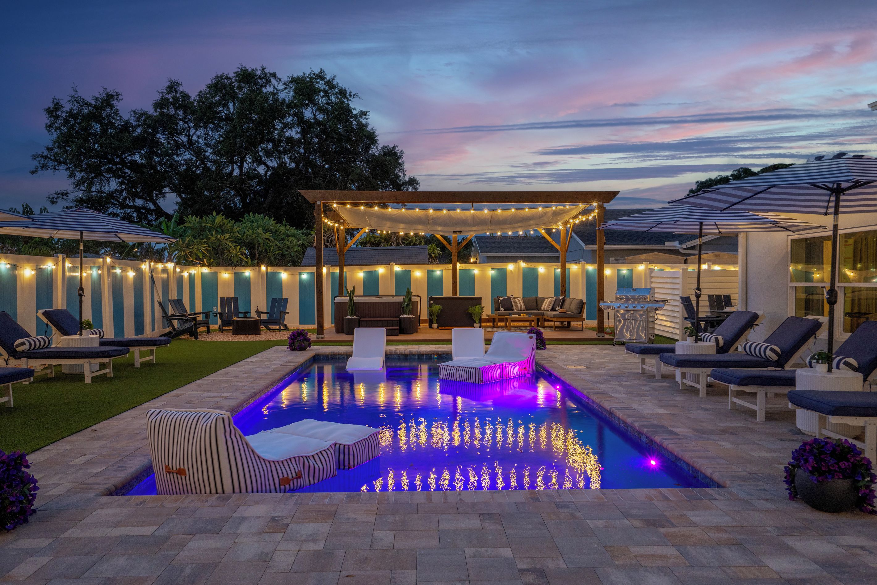 Un jardin avec une piscine, des chaises longues et des guirlandes lumineuses.