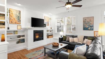 A living room with a fireplace, a television, a sofa, and a ceiling fan.