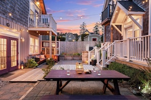 A wooden deck with a picnic table, surrounded by houses with balconies and string lights. - Sandbar Lodge: Carriage houseGame Rm, Pool+Gym access, Hot tub, Activity Garage (Lincoln City)