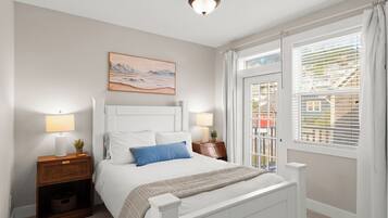 A bedroom with a bed, bedside lamps, a nightstand, a window with blinds, and a painting on the wall.