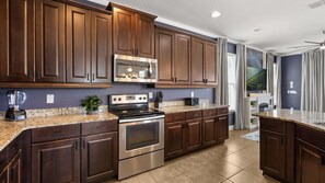 A modern kitchen with dark wood cabinets, stainless steel appliances, and a granite countertop. - Encore Resort Luxury 5BR: Private Pool & Game Room (Kissimmee)