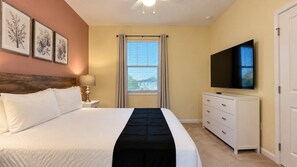 A bedroom with a bed, a TV, a dresser, a window with curtains, and framed artwork on the wall. - Bellavida Resort 12BR Mega-Villa | Sleeps 24 (Kissimmee)
