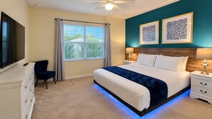 Ein Schlafzimmer mit Bett, Nachttischen, Fernseher, Sessel und Bildern an der Wand.