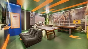 Ein Zimmer mit Billardtisch, Sitzsäcken, einem Wandgemälde von Dinosauriern und einem Schild mit der Aufschrift 'Bitte Dinosaurier nicht füttern'.