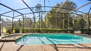 Ein Schwimmbecken mit Glasüberdachung, umgeben von einer Ziegelterrasse und Grünflächen.