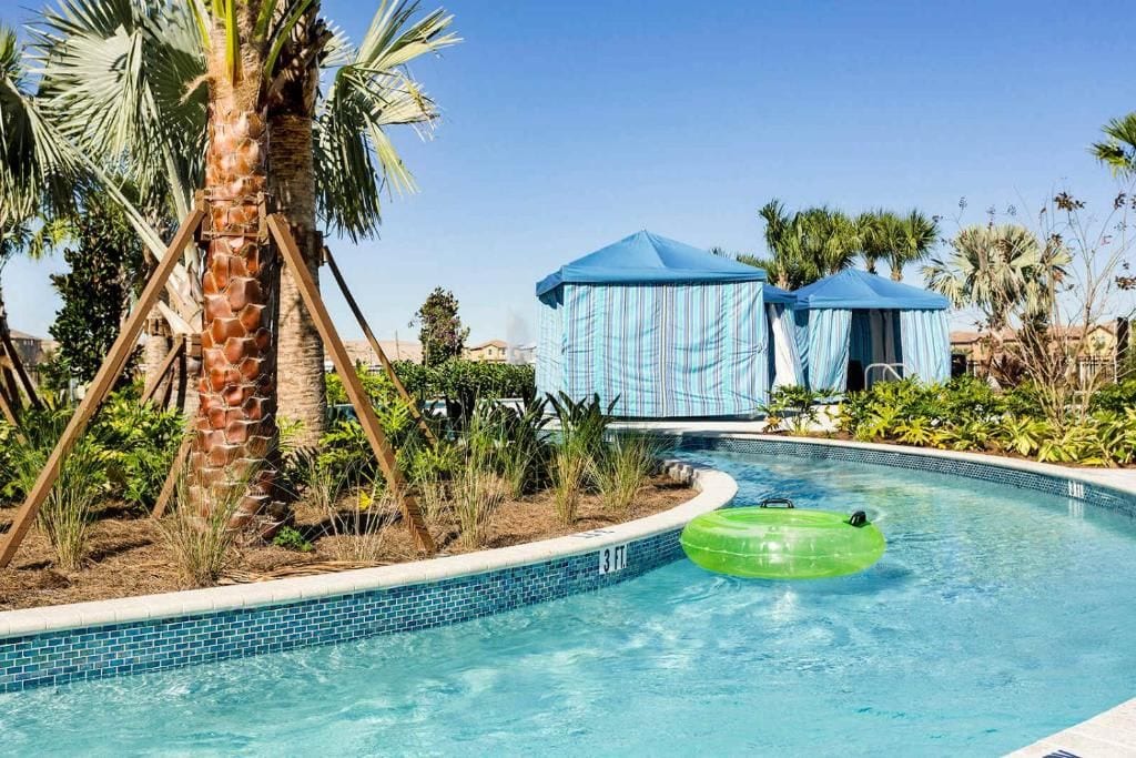 Une piscine avec un palmier, un tube gonflable vert et une tente bleue.