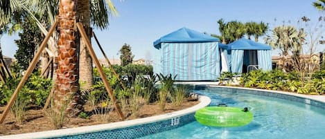 A swimming pool with a palm tree, a green inflatable tube, and a blue tent.