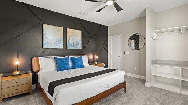 A bedroom with a bed, bedside tables, a ceiling fan, artwork on the wall, a mirror, and built-in shelving. - Lakeview 15BR Mansion • Pool, Cinema, Games Room (Kissimmee)