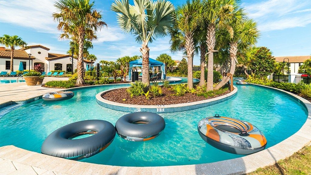 A swimming pool with three inflatable rings, surrounded by palm trees and lounge chairs.