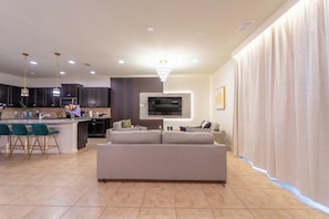 A modern living room with a sofa, a TV mounted on the wall, and a kitchen area in the background. - Royal Magic Villa • 10BR at Windsor Resort (Kissimmee)
