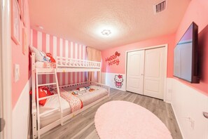Een kinderkamer met stapelbedden, een Hello Kitty muursticker, een rond roze vloerkleed en een witte deur.