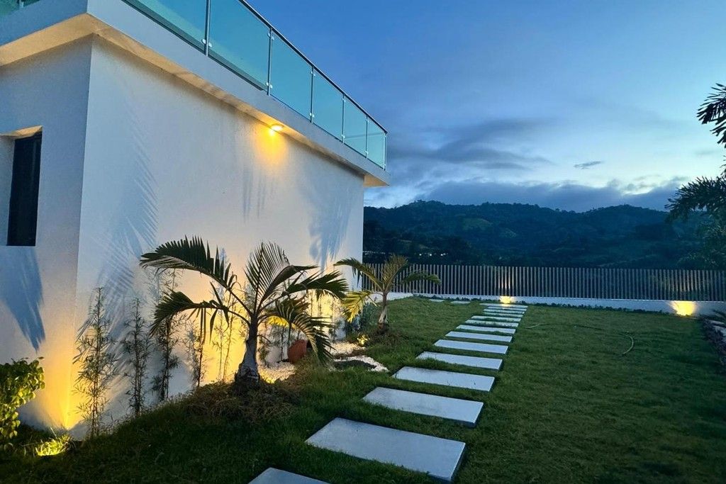 Un bâtiment moderne doté d’un balcon en verre, d’une pelouse bien entretenue et d’un chemin de pierre menant à l’entrée.