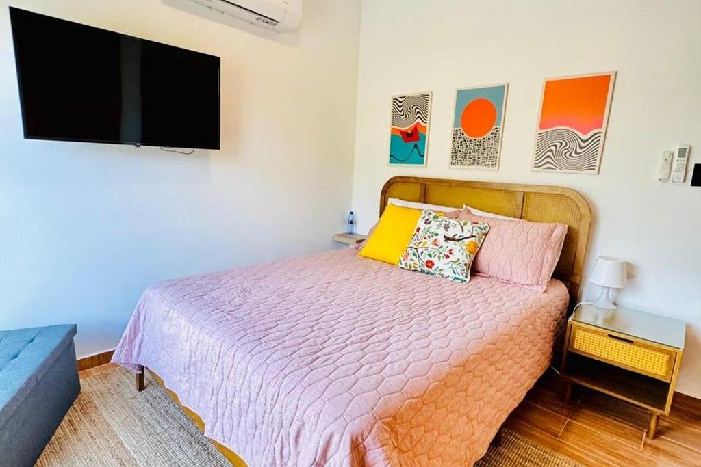 A bedroom with a bed, a bedside table, a wall-mounted TV, and three wall art pieces.