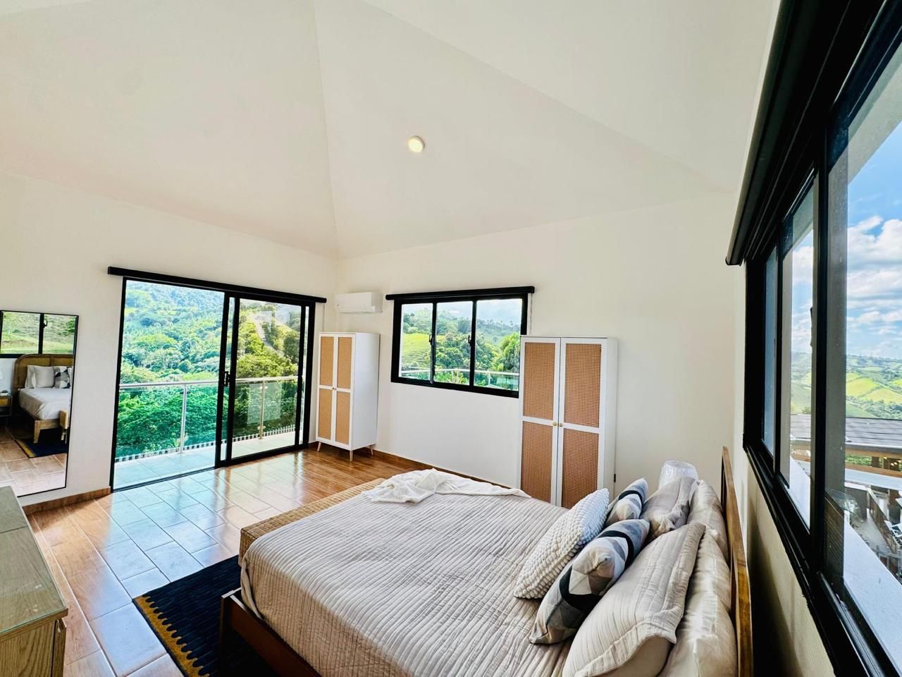 Une chambre dotée d’un grand lit, d’une armoire et offrant une vue sur un paysage verdoyant grâce à de grandes fenêtres.
