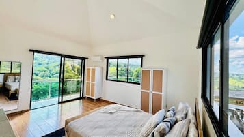Une chambre dotée d’un grand lit, d’une armoire et offrant une vue sur un paysage verdoyant grâce à de grandes fenêtres.