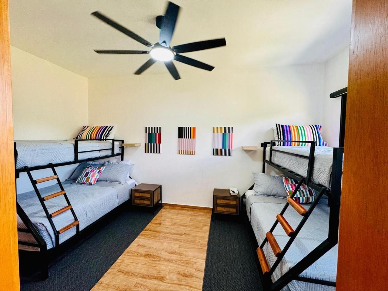 Une chambre avec des lits superposés, un ventilateur de plafond et une petite table avec une lampe.