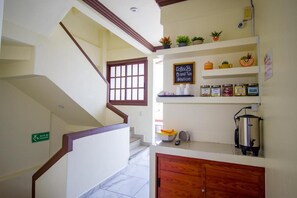 Una escalera conduce a un espacio con estación de café y té, con estantes llenos de frascos y una máquina de café.