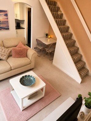 Ein Wohnzimmer mit einer Couch, einem Couchtisch mit einer Schale, einer Treppe und einem Essbereich mit Tisch und Stühlen.
