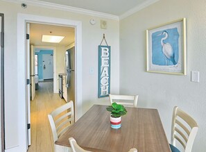 A dining area with a wooden table, white chairs, and a potted plant. - 1BR Oceanfront Suite, Wake Up to the Atlantic! (Myrtly Beach)