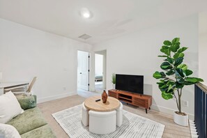 A modern living room with a sofa, a coffee table, a TV, and a potted plant. - Modern 3BR Townhome Near Stonecrest (Lithonia)