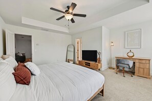 A bedroom with a bed, a TV, a desk, and a ceiling fan. - Modern 3BR Townhome Near Stonecrest (Lithonia)