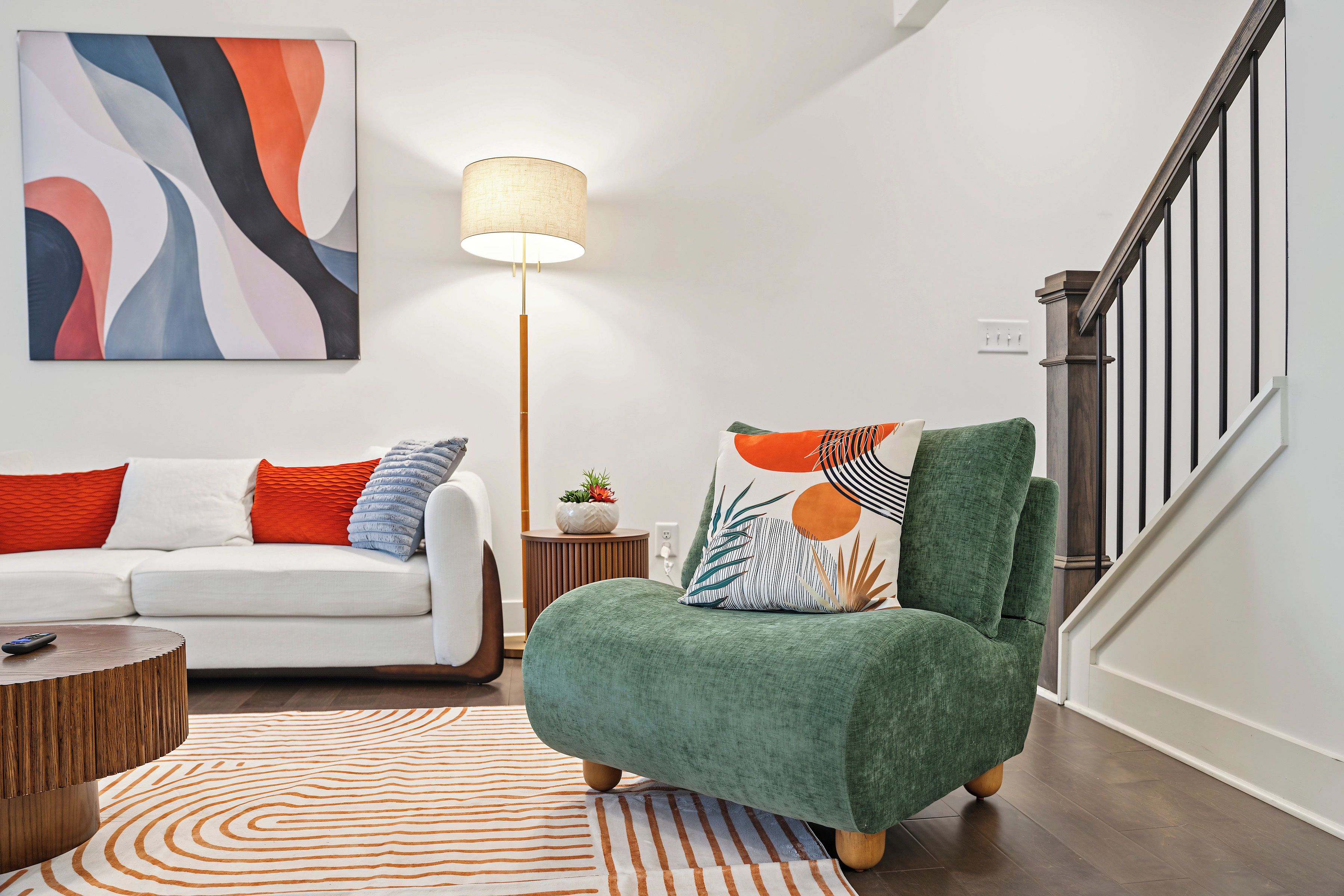 A modern living room with a sofa, a green armchair, a lamp, and a patterned rug.
