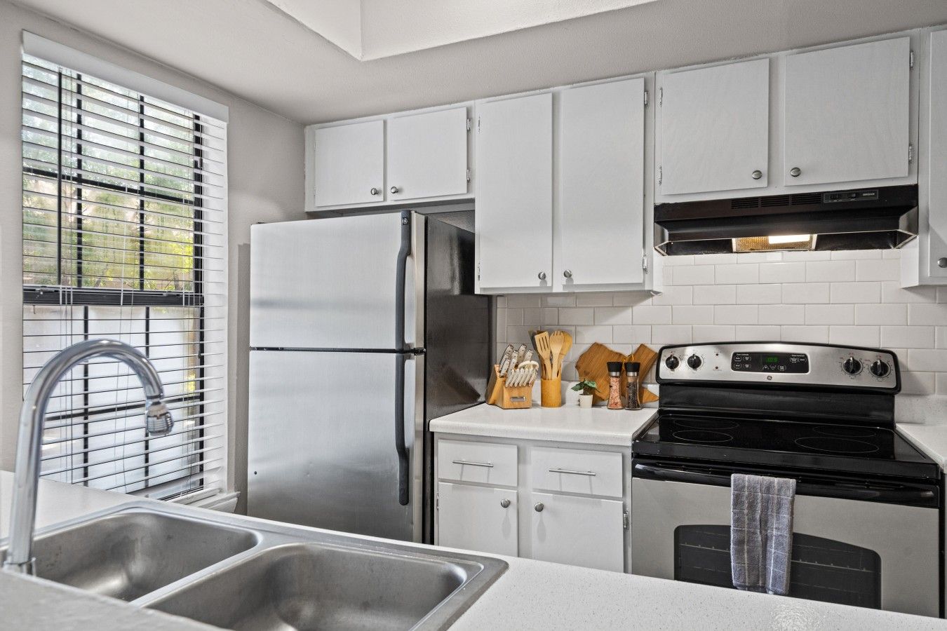 A modern kitchen with stainless steel appliances, white cabinetry, and a window with blinds.