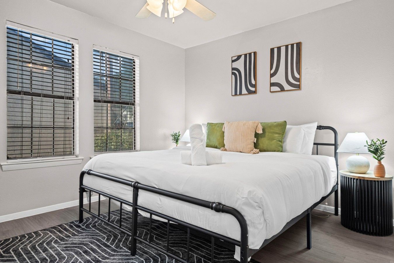 A bedroom with a bed, a bedside table, a lamp, and a window with blinds.