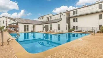 Piscina com espreguiçadeiras e um edifício com fachada branca.