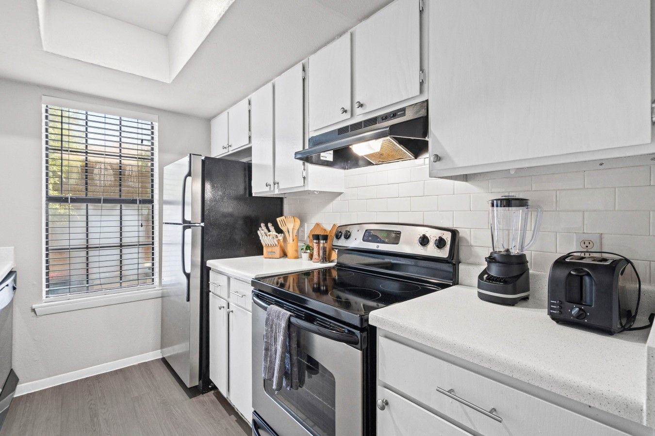 A modern kitchen with white cabinets, a black stove, a blender, and a toaster.