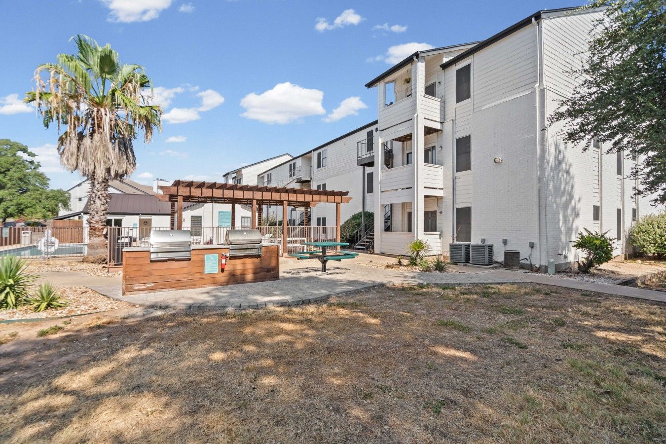 A residential building with a covered outdoor seating area, a pool, and a well-maintained lawn.