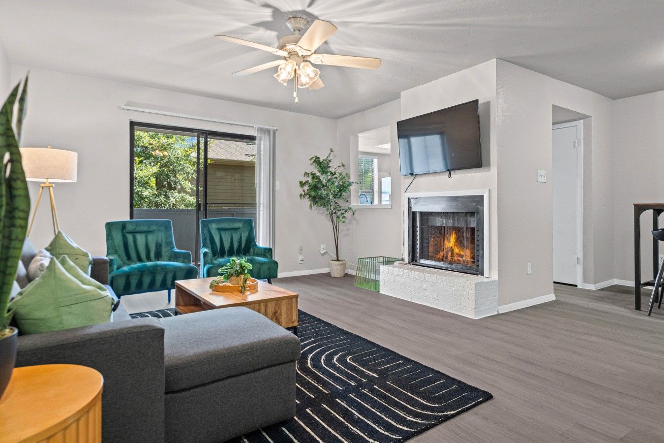 A modern living room with a fireplace, green chairs, a coffee table, and a ceiling fan.