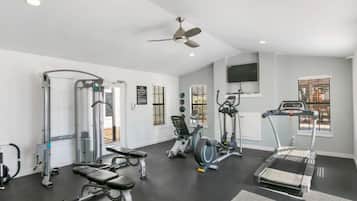 Uma academia com diversos equipamentos de exercício, um ventilador de teto e uma televisão na parede.
