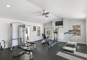 Un gimnasio con diversos equipos de ejercicio, un ventilador de techo y un televisor en la pared.
