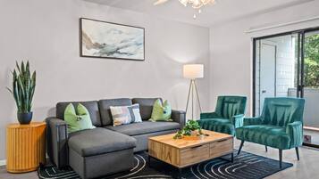 A modern living room with a grey sofa, a wooden coffee table, and teal armchairs.