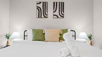 Cama bem arrumada com uma toalha enrolada, duas almofadas e um edredom. Duas pinturas abstratas estão penduradas na parede acima da cama.