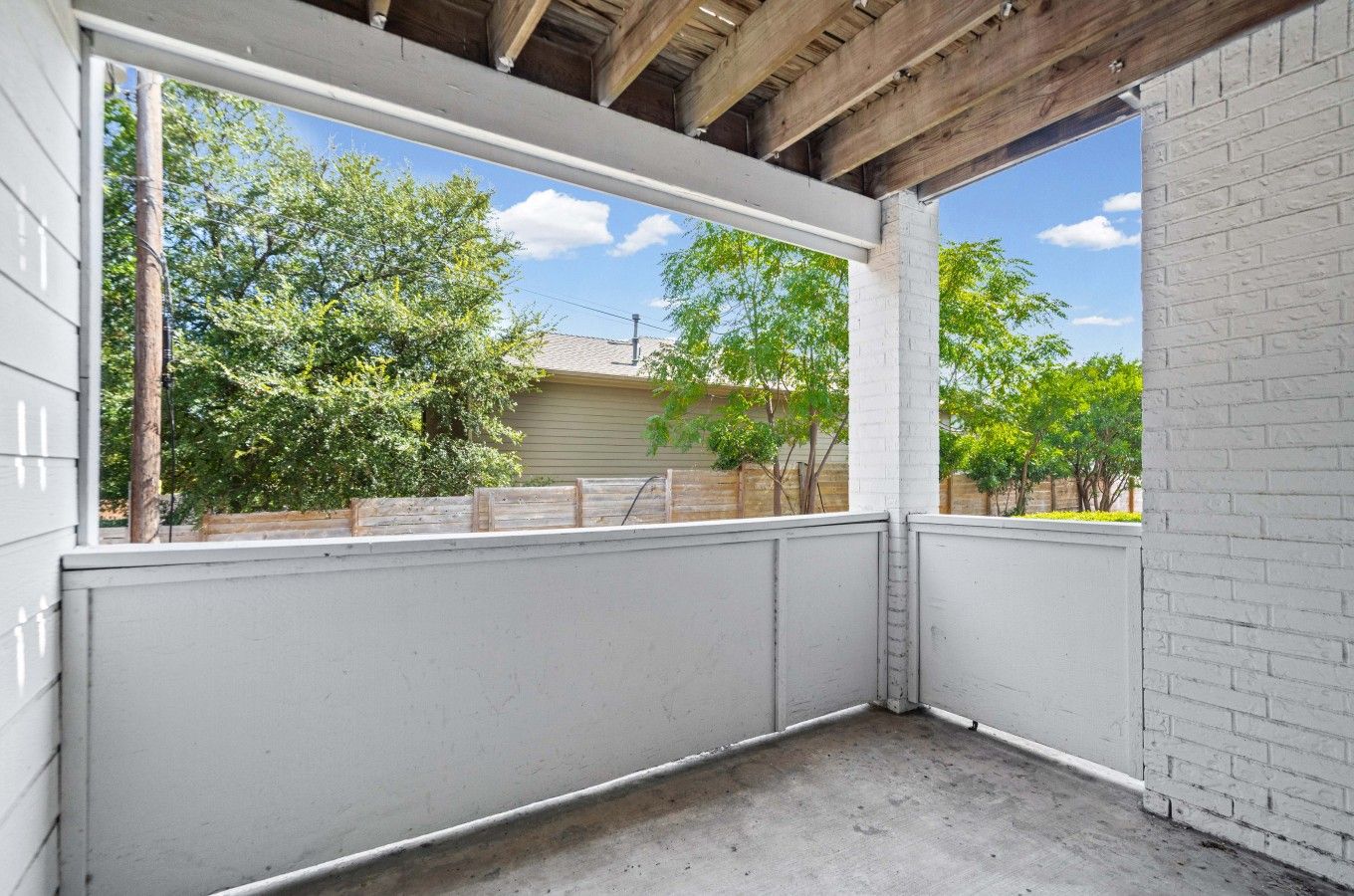 A covered outdoor area with a concrete floor, white walls, and a wooden ceiling.