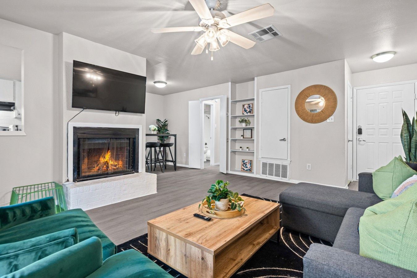 A modern living room with a fireplace, a ceiling fan, and a flat-screen TV.