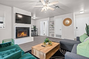 Una sala de estar moderna con chimenea, ventilador de techo y televisor de pantalla plana.