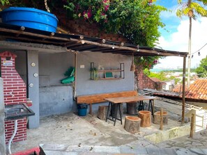 Un espacio de descanso al aire libre rústico con un banco y una mesa de madera, rodeado de árboles y un depósito de agua azul.