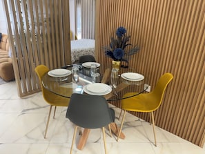 A dining area with a glass table, yellow chairs, and a vase with blue flowers. - New Luxury 3-Bedroom Apartment (Casablanca)