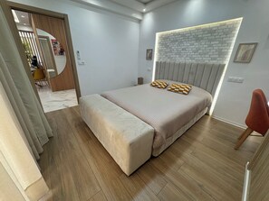 A bedroom with a large bed, a wooden floor, a modern headboard, and a dining area visible through a doorway. - New Luxury 3-Bedroom Apartment (Casablanca)