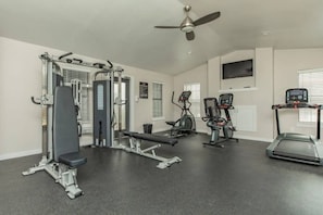 Ein Fitnessraum mit Trainingsgeräten, einem Deckenventilator und einem Fernseher an der Wand.