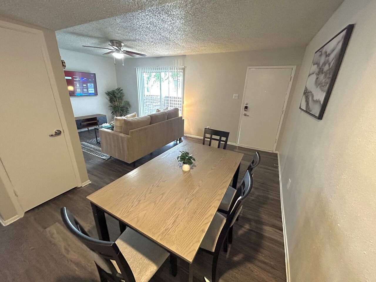 A dining area with a wooden table and chairs, a ceiling fan, and a view of a living room with a couch and a TV.