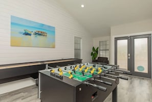 Ein Kicker steht in einem Raum, an der Wand hängt ein Gemälde mit Booten, es gibt eine Pflanze und eine Tür mit Fenster.
