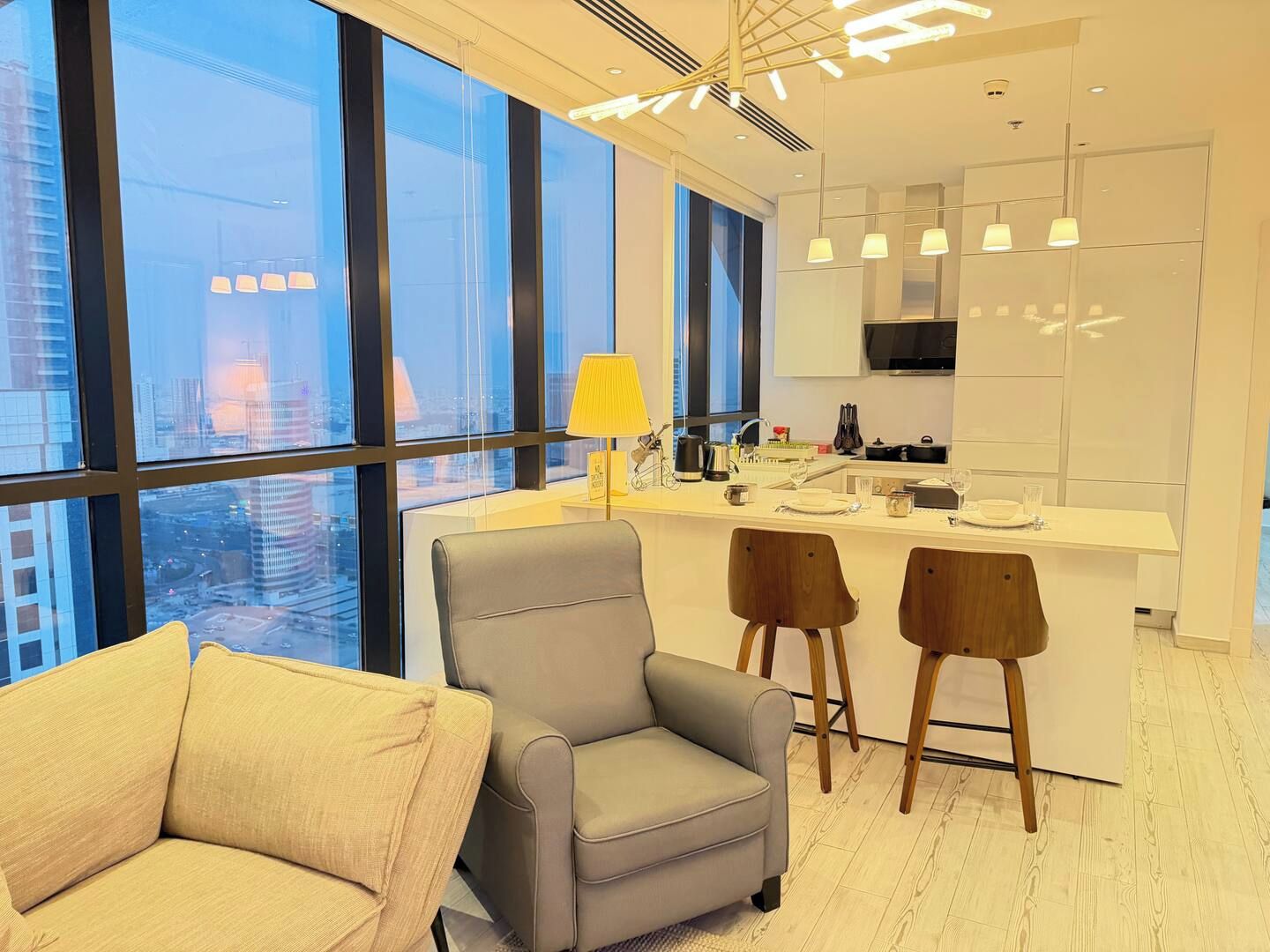 A modern interior with a sofa, two chairs, a kitchen island, and large windows.