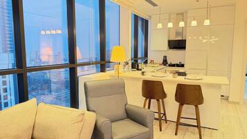 A modern interior with a sofa, two chairs, a kitchen island, and large windows.