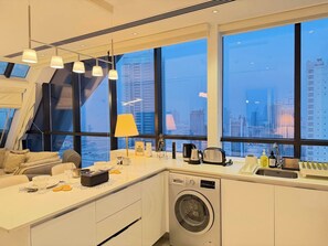Una cocina moderna con lavadora integrada, ventanas amplias que ofrecen vistas a la ciudad y un comedor con una mesa dispuesta para dos.